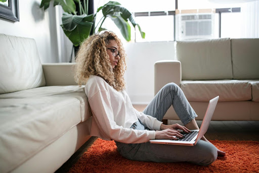 Woman is looking at her laptop. She is sitting on the ground in her home